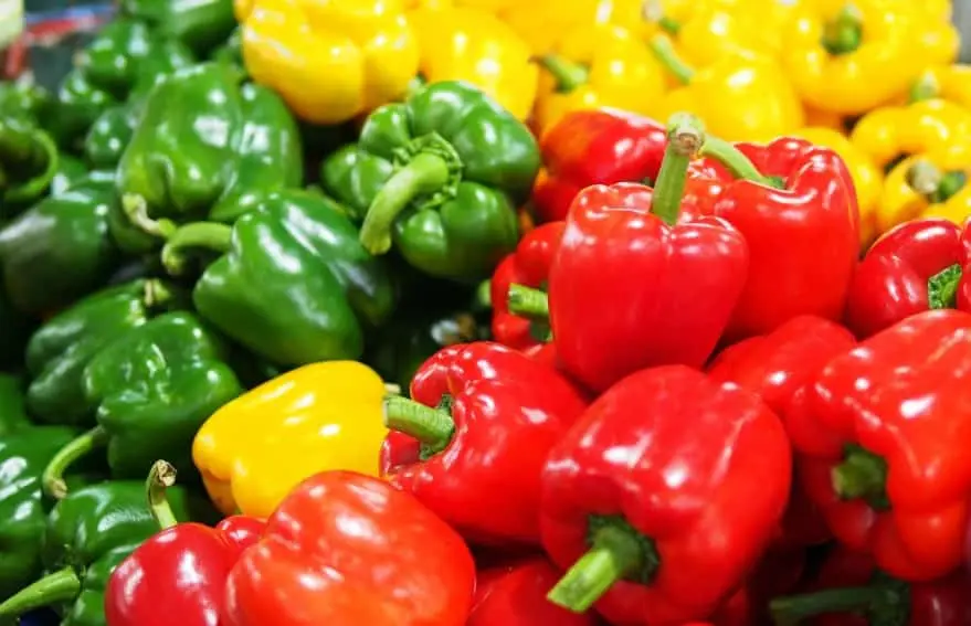 Peperoni freschi rossi, gialli e verdi su un tagliere di legno, ricchi di vitamine e proprietà antiossidanti
