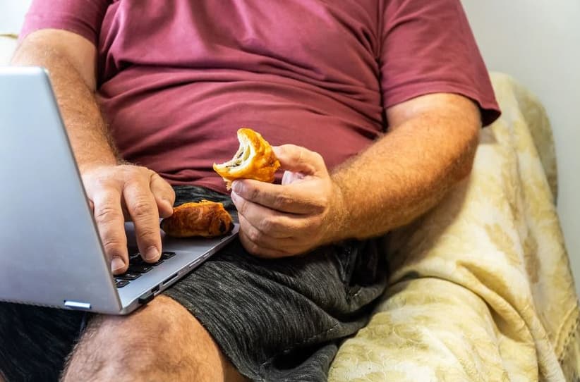 Uomo sovrappeso che mangia seduto al computer