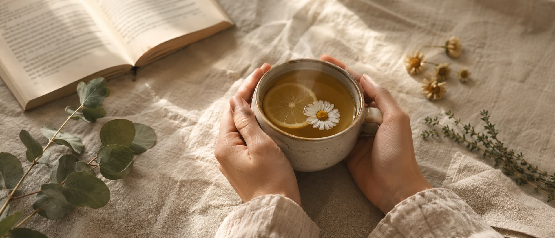 Mani che tengono una tazza di tisana fumante con camomilla, limone ed erbe officinali su tavolo di lino, simbolo della cura quotidiana e del benessere secondo la guida alla salute di Leaderfarma Blog