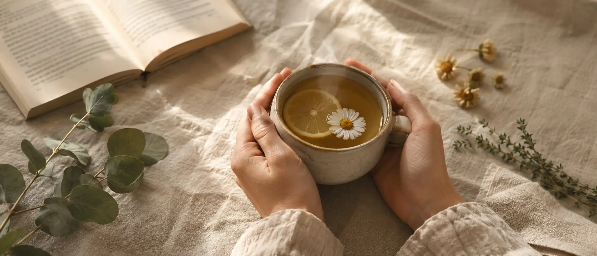 Mani che tengono una tazza di tisana fumante con camomilla, limone ed erbe officinali su tavolo di lino, simbolo della cura quotidiana e del benessere secondo la guida alla salute di Leaderfarma Blog