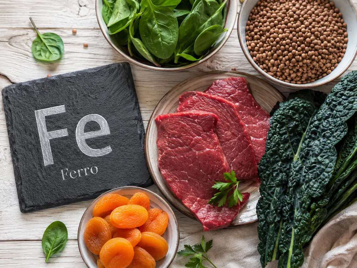 Carne rossa, spinaci e legumi fonte di ferro accanto al simbolo chimico Fe.